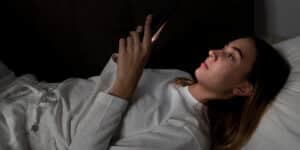 Persona en cama usando teléfono inteligente a oscuras